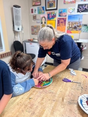 ITC Docent Ellen Brooker works with a Mark Twain student working on a paper-plate loom.