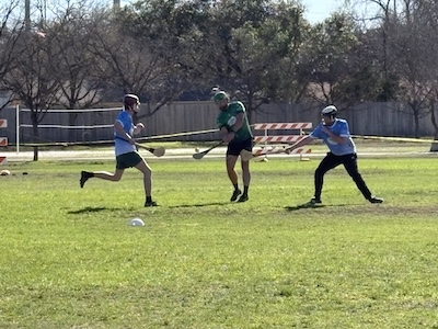 A hurler attempts to pass the sliotar across the field with a strike from his hurley.