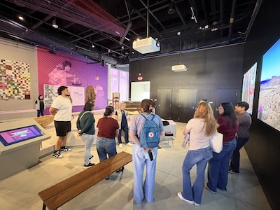 Docent Paulette Brient meets with Community Translations students at her usual post on the ITC exhibit floor.