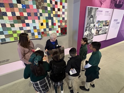 Docent Joanne Duming welcomes St. Gregory the Great students on the ITC exhibit floor. Duming often discusses sharecropping and quilting in her presentations for museum visitors.